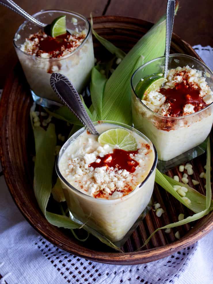 Elote en Vaso / Esquites (Corn in a Cup) cups on a platter with corn drizzled with hot sauce