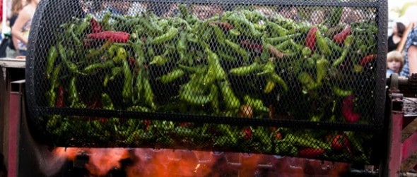 pueblo green chiles being roasted over flame in a big black cylindrical metal container