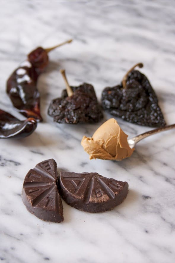 two kinds of dried mexican chiles, a spoonful of peanut butter and a round of abuelita chocolate on a marble surface