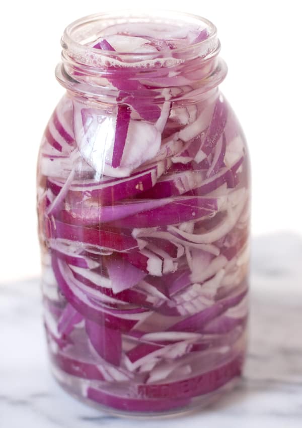 mason jar filled with sliced onions and hot water as part of making the recipe for Mexican pickled red onions.