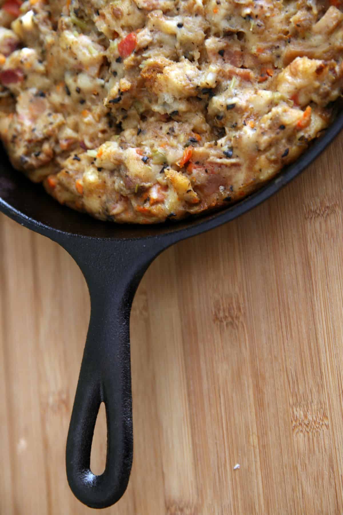 a black cast iron skillet with homemade Thanksgiving stuffing on a wooden table.