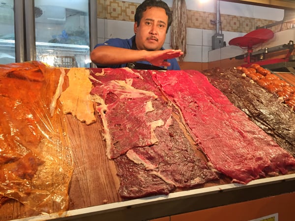 Mexican man in Oaxaca mercado market selling a selection of meats for taquiza carnes