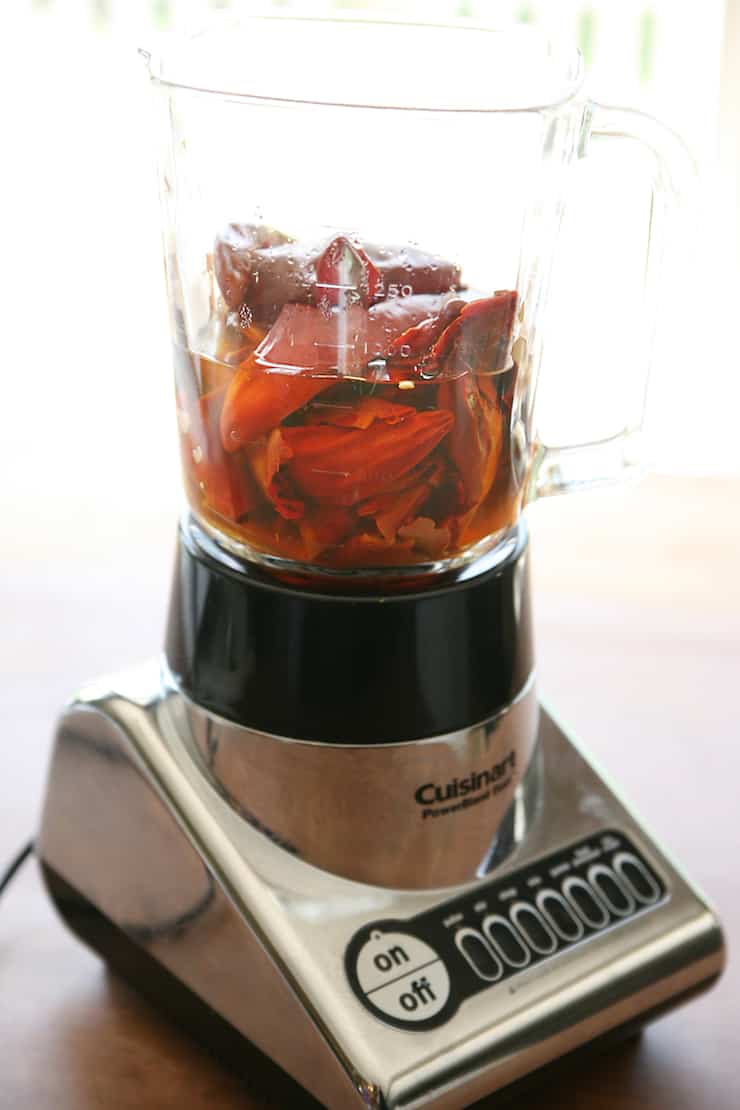 silver blender filled with whole red chiles and other ingredients for homemade enchilada sauce