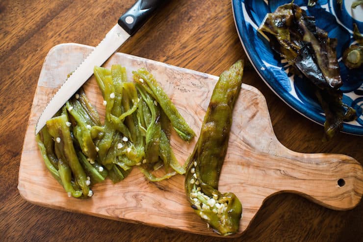 roasted hatch green chiles in a bowl with one sliced on a wooden cutting board with a sharp knife