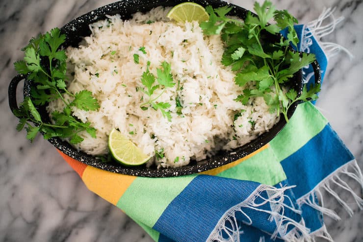 overhead shot of a serving bowl of Cilantro lime rice garnished with fresh coriander leaves and lime slices on a marble table