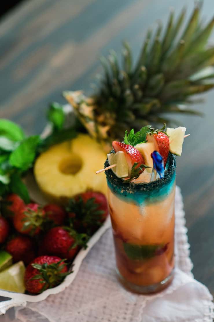 close up a pineapple and strawberry mojito garnished with fresh fruit on a skewer