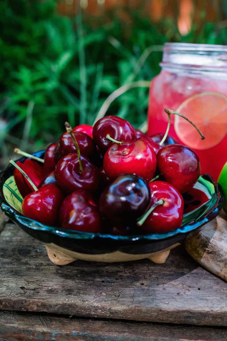 Delicious fresh cherries in a bowl with a jar full of the cold drink in the back