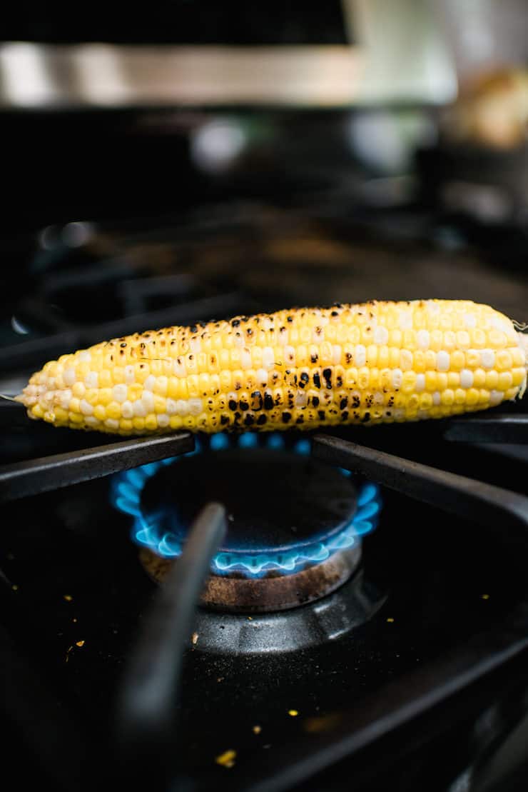 corn on the cob being roasted on a cast stovetop indoors