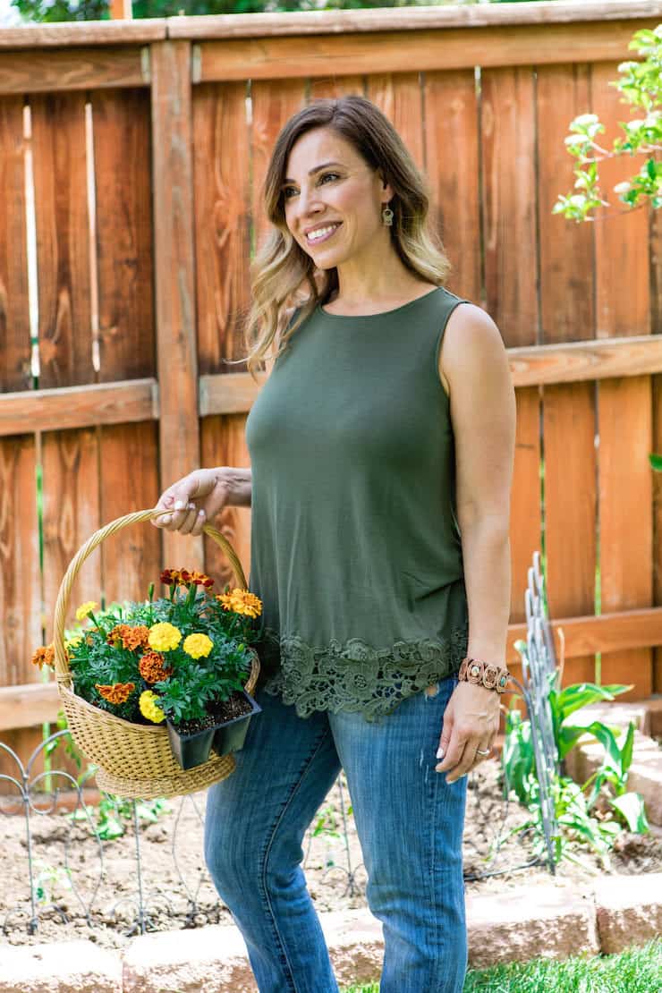 Latina lifestyle blogger holding a basket of yellow and orange marigolds to plant in home garnden