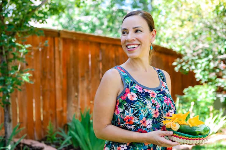 latina blogger holding basket of squash blossoms in the garden