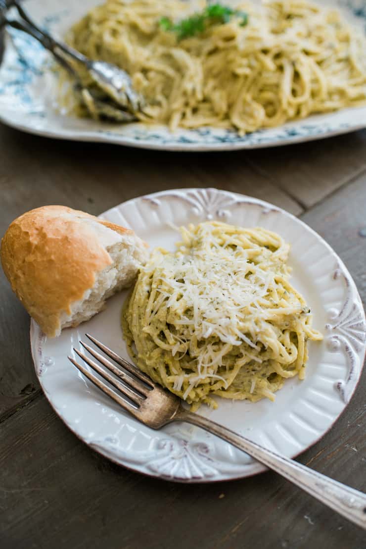 serving of Espagueti Verde (Spaghetti with Creamy Poblano Sauce) on a white plate with a piece of bread.