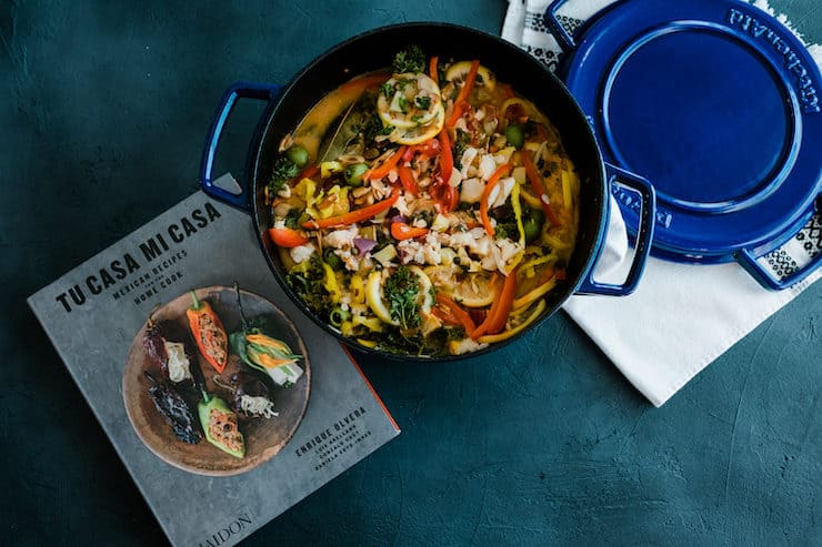 veracruz style seafood stew in a blue enameled pot, alongside the cookbook Tu Casa Mi Casa