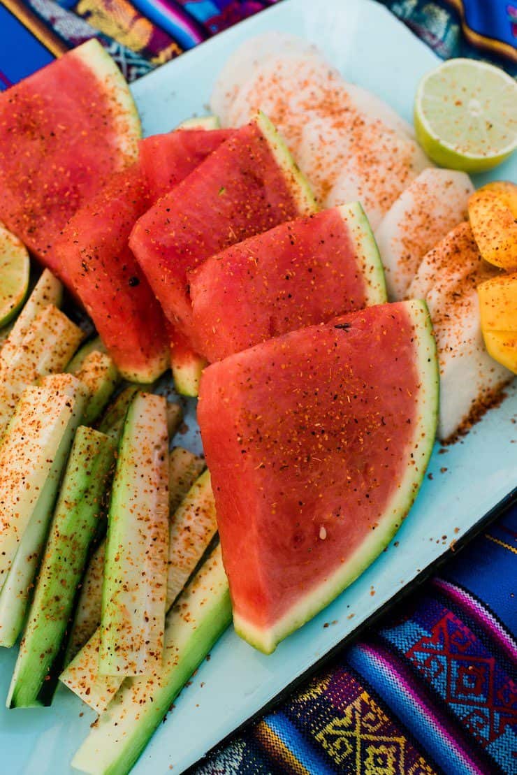 fruit slices sprinkled with chili powder on a teal platter on a Mexican runner