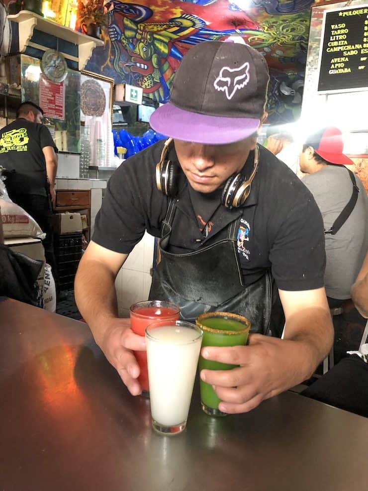 guy wearing headphones and a ball cap serving three different flavored pulques at Pulquería Las Duelistas