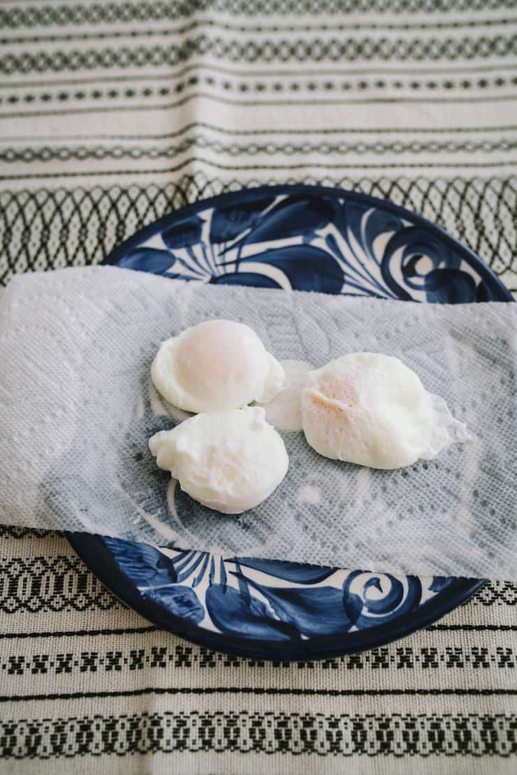 three poached eggs on a paper towel lined plate for eggs Benedict 