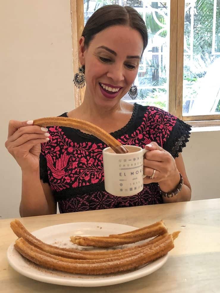 Foddering blogger wearing a black and pink embroidered dress from Mexico dipping churros in hot chocolate at Churrería El Moro