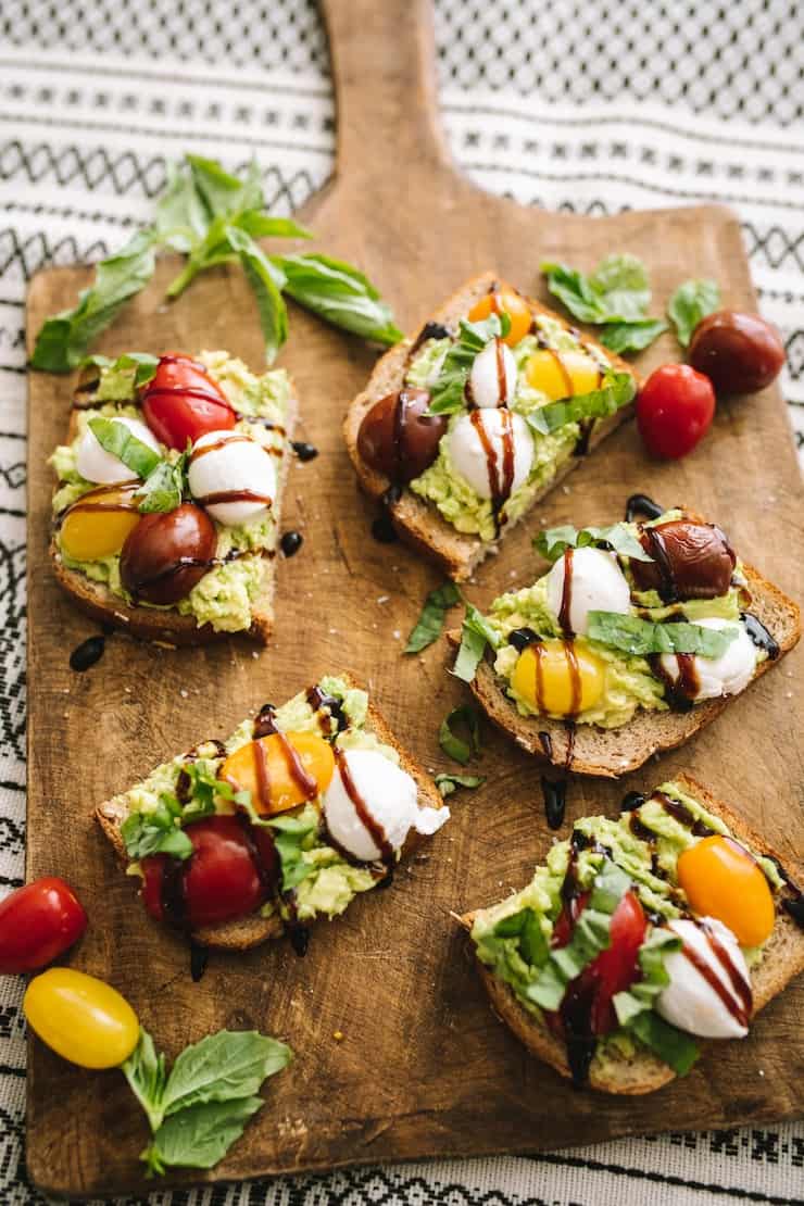 Healthy and delicious Caprese Avocado Toast with cherry tomatoes and basil on the board