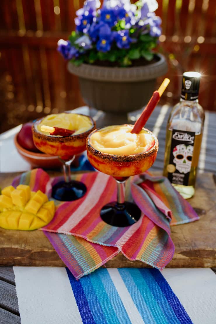 mango frozen Margaritas with exotico tequila in background and colorful Mexican textiles
