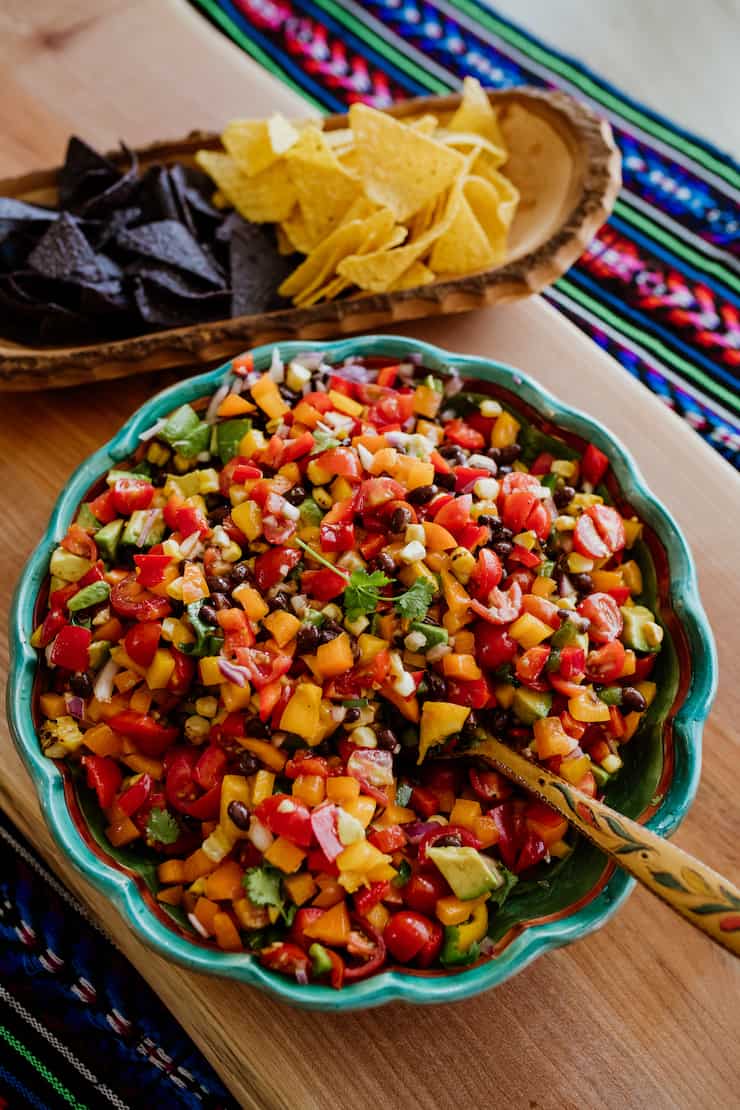 cowboy caviar in a teal bowl with wooden spoon served with blue and yellow corn chips