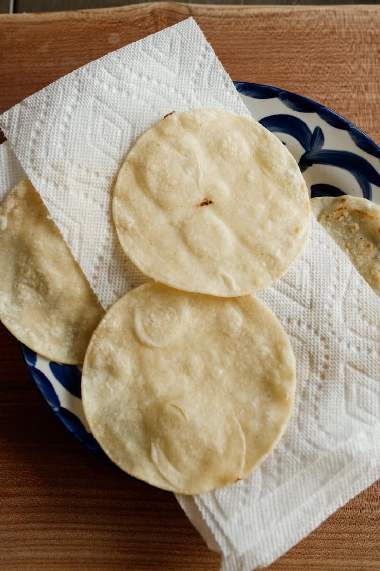 lightly fried corn tortillas draining on paper towels on a Mexican pottery plate