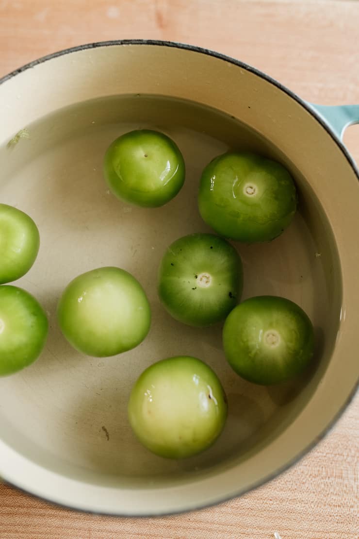 Eight raw tomatillos in water ready to boil