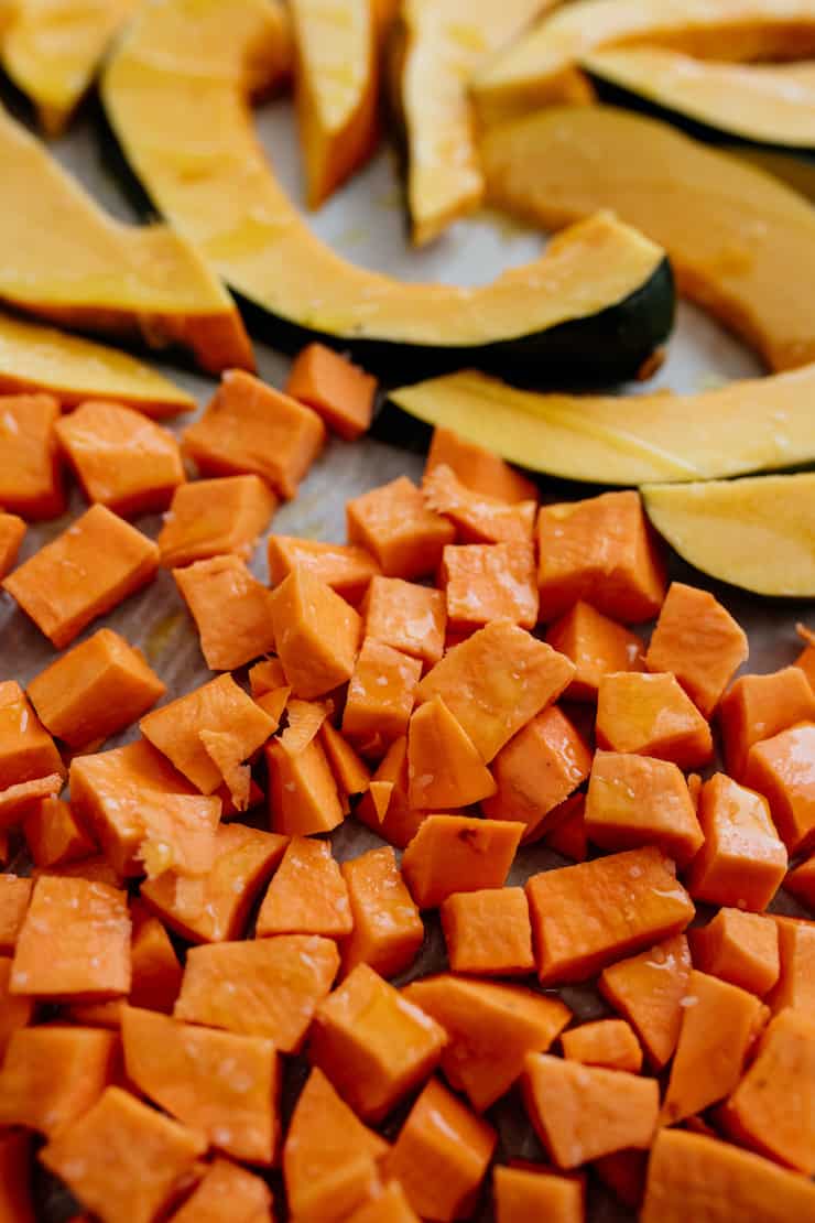 sweet potato cubes and acorn squash slices on a parchment lined sheet pan prior to baking.