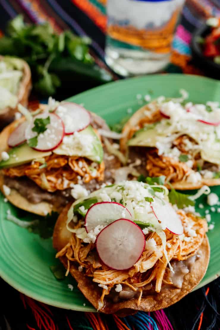 Chicken Tinga tostadas with refried beans on a green plate