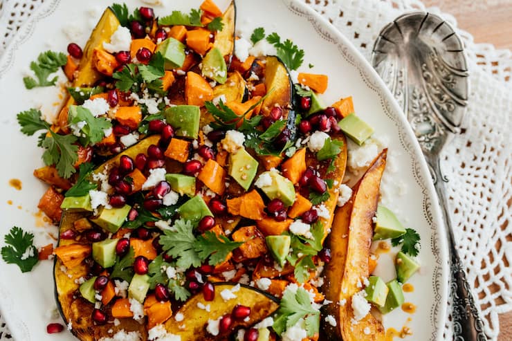 finished winter salad with roasted sweet potatoes, acorn squash, fresh avocado, bright pomegranate arils and fresh cilantro on a white serving platter