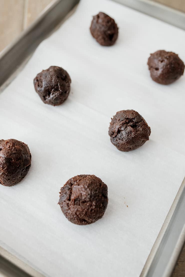 chocolate cookie dough balls on a parchment lined baking sheet