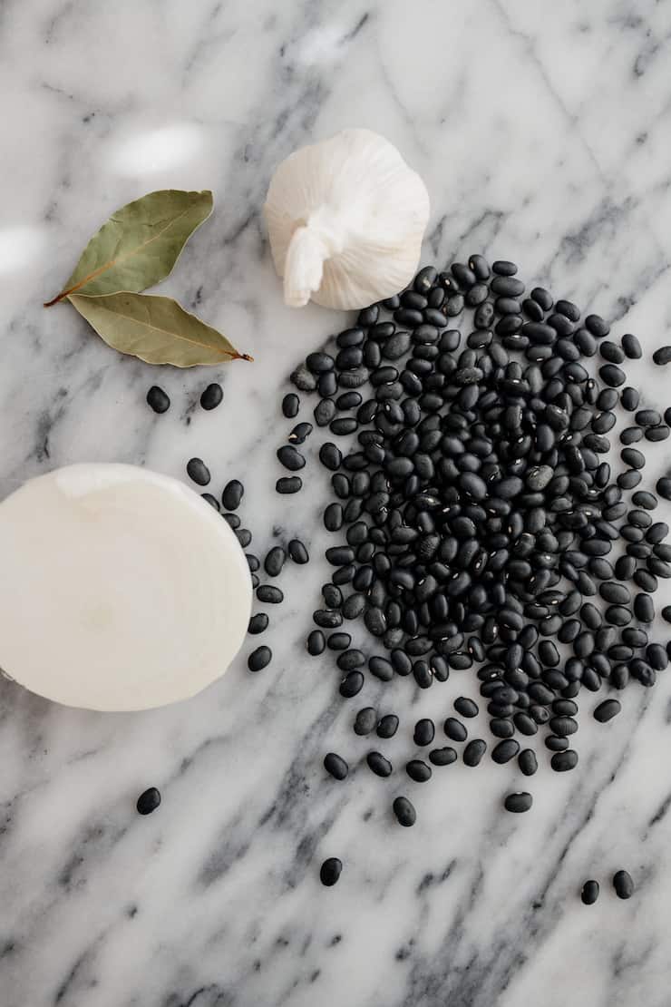 black beans, onion, garlic and bay leaf on grey and white marble surface