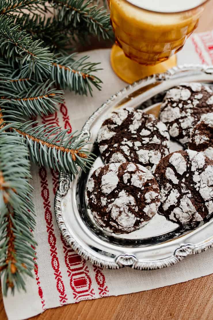 mexican chocolate crinkle cookies on a silver platter with a branch of a pine tree