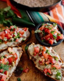 molletes with refried beans, melted cheese and colorful pico de gallo on a wooden cutting board