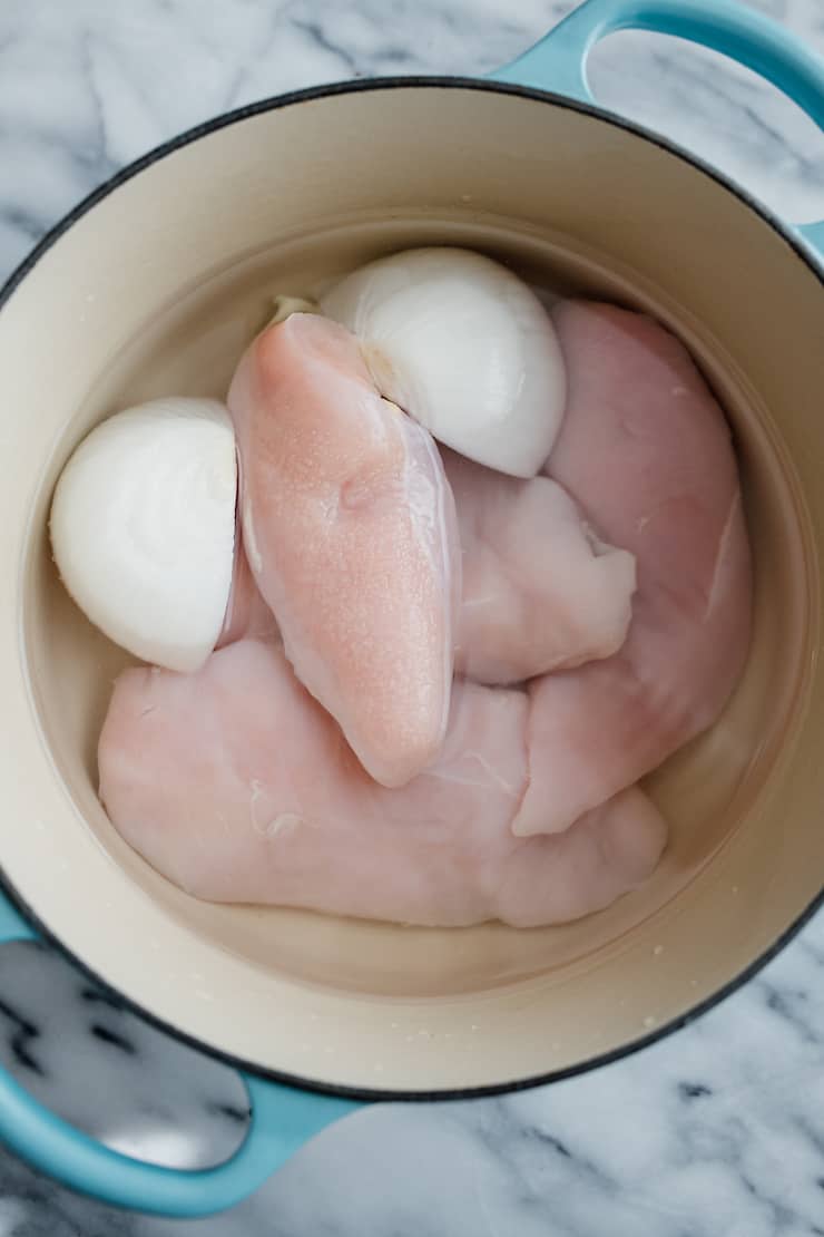 raw chicken breasts and a white onion that has been halved in water in an enameled cast iron pot