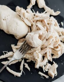 Poaching chicken breast with a metal fork on a dark plate