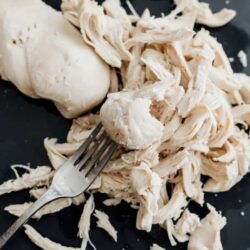 Poaching chicken breast with a metal fork on a dark plate