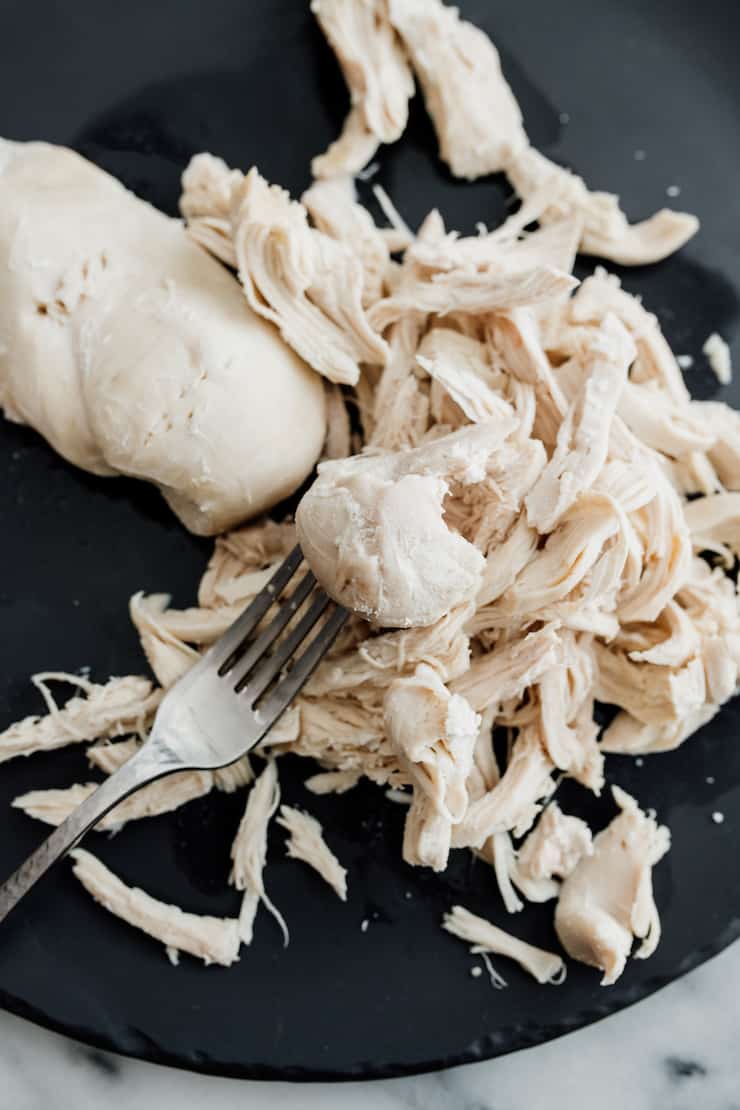 poached chicken breasts on a black plate with one shredded and a silver fork