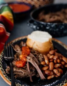 shredded crockpot brisket on a black plate with beans, bolillo and salsa