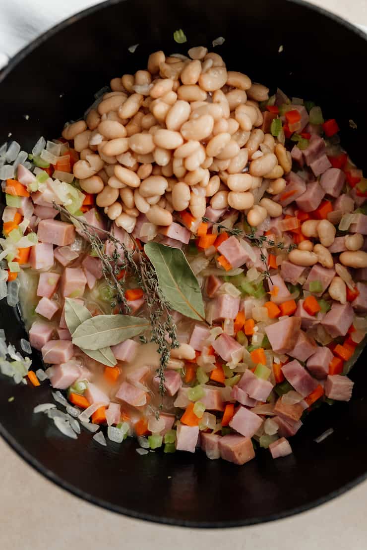 beans and herbs added to pot with ham and mirepoix