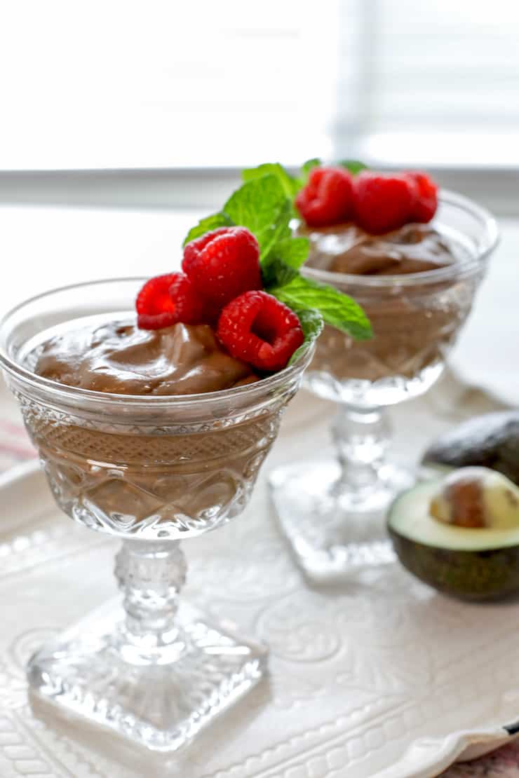 two crystal glasses filled with mexican chocolate avocado pudding and garnished with raspberries and mint