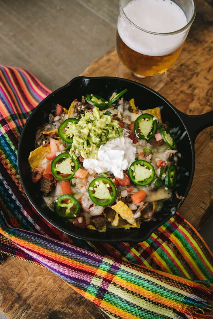 overhead shot of brisket nachos in a cast iron skillet garnished with jalapeños, sour cream and guacamole
