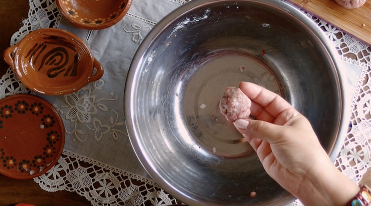 hand rolling a single albondiga above a silver mixing bowl on a white lace doily