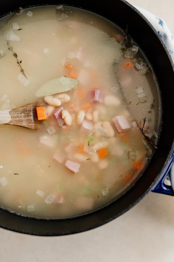 overhead shot of completed ham and white navy bean soup in pot with wooden spoon