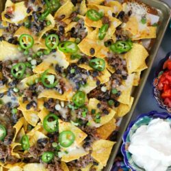 overhead shot of classic sheet pan nachos with several bowls of toppings on the side