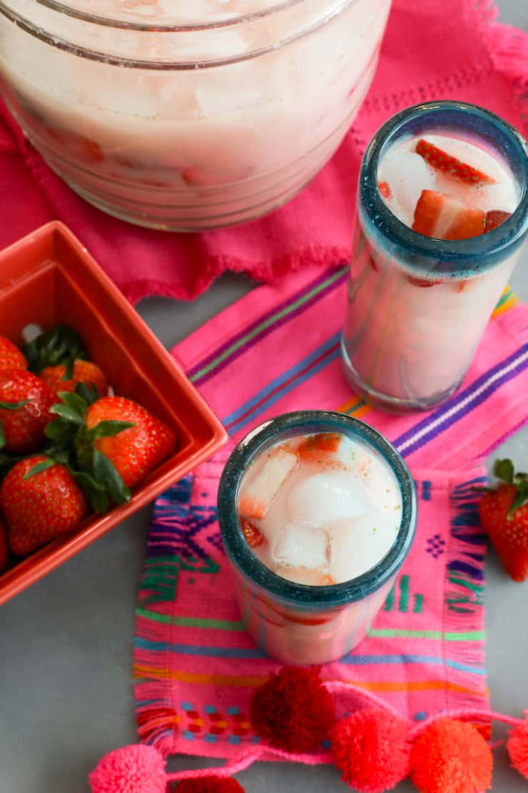 overhead shot of homemade strawberry horchata in glasses garnished with fresh strawberry slices on bright pink and blue striped fabric