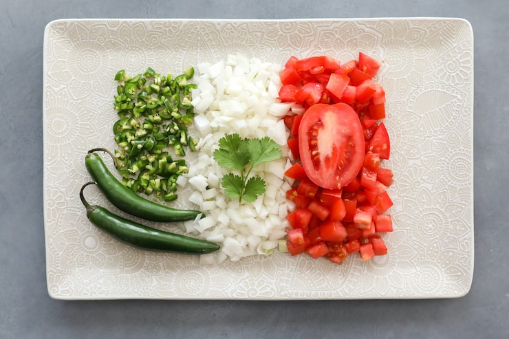 chiles, onions and tomatoes arranged to look like the Mexican flag on a white rectangular plate with a sprig of fresh cilantro