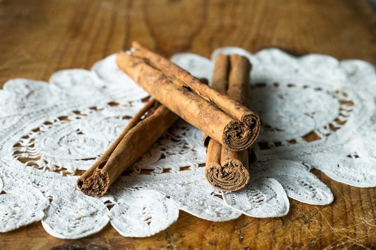 three cinnamon sticks on a vintage doily on wooden surface