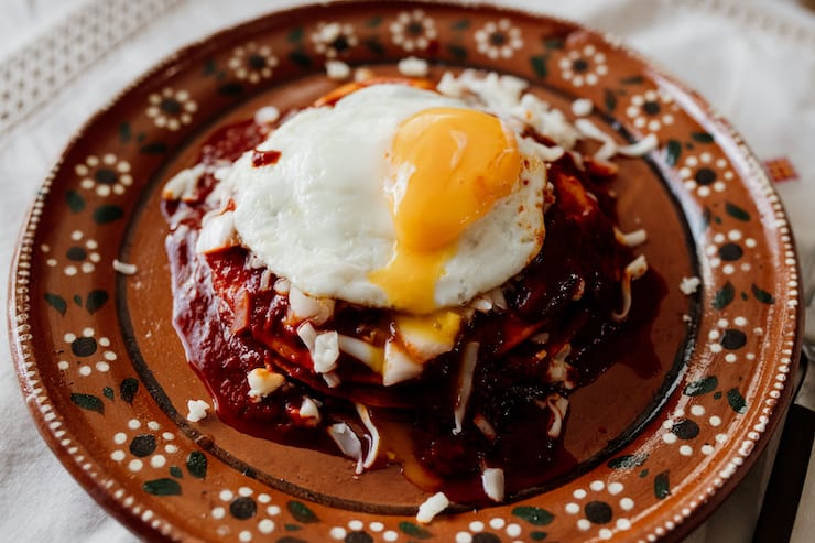stacked red enchiladas on an earthenware plate with a fried egg on top