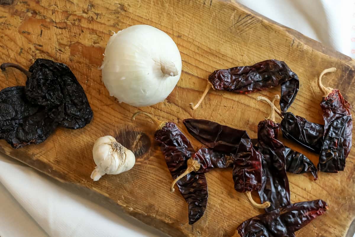 dried chiles and a fresh onion with a head of garlic on a wooden board