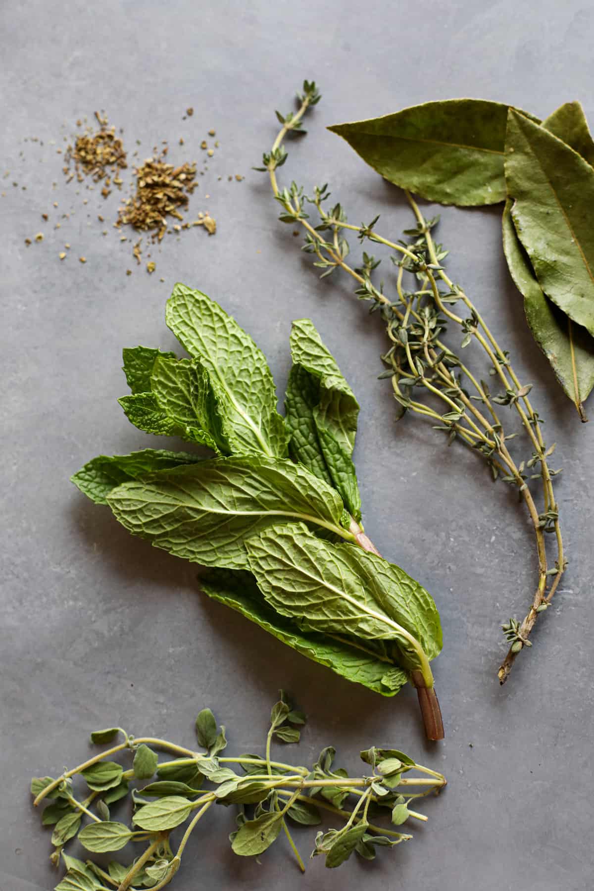 fresh mint, thyme, oregano and bay leaves on a gray background