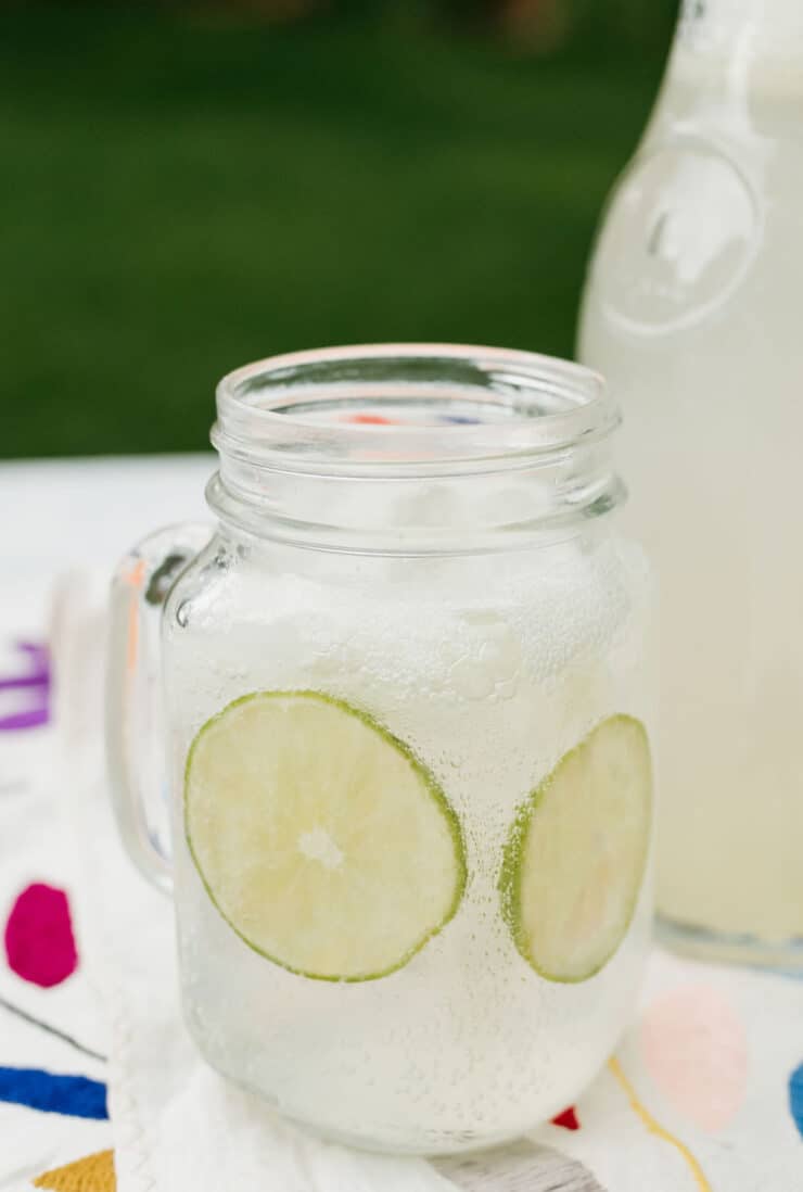 mason jar filled with sparkling limeade with a carafe of the limonada in the background